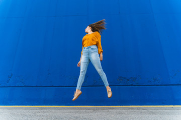 Young woman jumping against blue wall