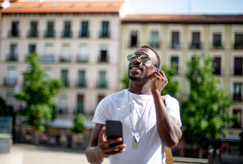 Smiling young man using smartphone and ear phones, looking up
