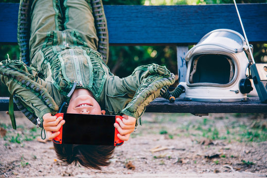 Fototapeta Boy wearing a space suit and, a bench, holding video game in front of his face