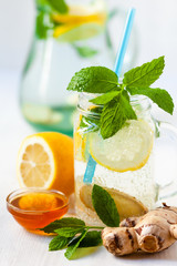 Healthy and tasty summer drink: homemade lemonade with lemon, mint, honey, ginger in transparent glass mug with blue straw. Healthcare, concious lifestyle, detox. White background, copy space for text