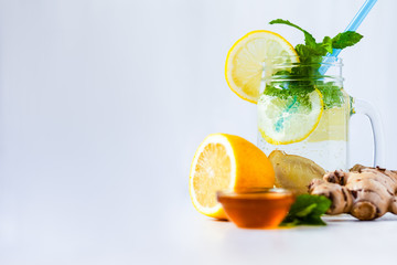 Healthy and tasty summer drink: homemade lemonade with lemon, mint, honey, ginger in transparent glass mug with blue straw. Healthcare, concious lifestyle, detox. White background, copy space for text