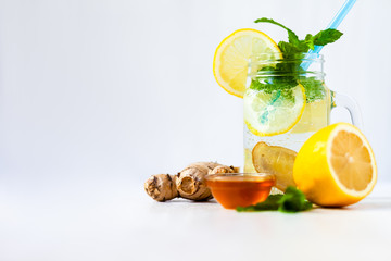 Healthy and tasty summer drink: homemade lemonade with lemon, mint, honey, ginger in transparent glass mug with blue straw. Healthcare, concious lifestyle, detox. White background, copy space for text