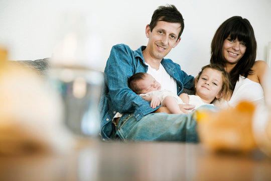 Young family with male newborn and little daughter sitting on sofa at home