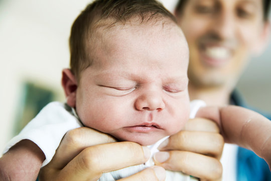 Smiling young father holding his sleeping newborn son