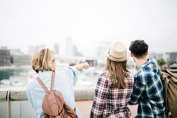 Spain, Barcelona, back view of three friends standing side by side pointing on something