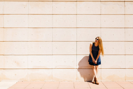 Happy woman leaning against wall in summer