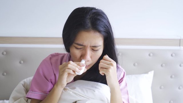 Sick woman sniffing nasal spray while sitting on the bed in bedroom at home. Shot in 4k resolution
