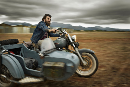 Man with full beard driving motorcycle with sidecar