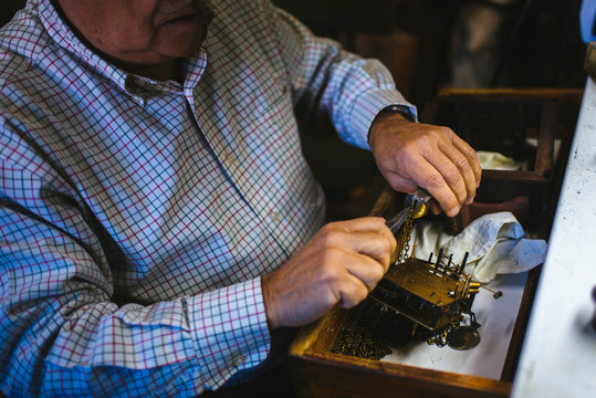 Watchmaker hands in the foreground working with an antique clock