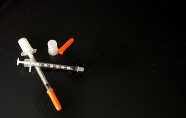 Two injection needles laying on a black background. One needle has the caps removed.