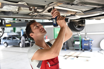 Car mechanic working in repair garage, repairing unterbody