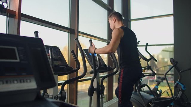 Portrait fitness man warm up before training on elliptical cross trainer in gym club. Close-up male training cardio exercise on cross trainer in fitness.