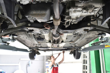 Car mechanic working in repair garage, checking underbody of a car