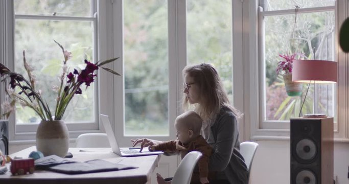 Single parent working from home and holding baby