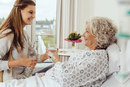 Granddaughter visiting grandmother in hospital, giving her glass of water