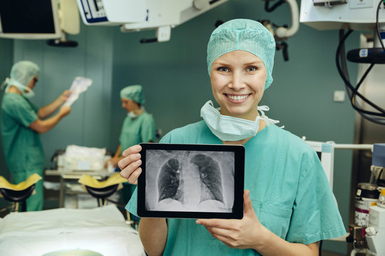 Smiling female surgeon in surgery room holding a digital tablet with a thorax x-ray image