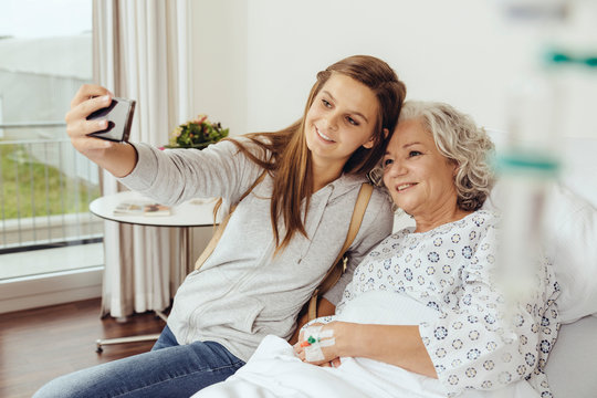 Granddaughter visiting grandmother in hospital, taking selfie with smart phone