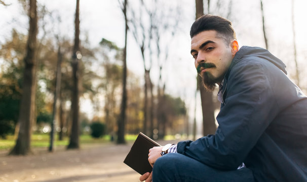 Portrait of bearded young man with book in the park