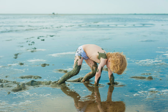 Germany, Schleswig Holstein, Boy playing in mud at beach