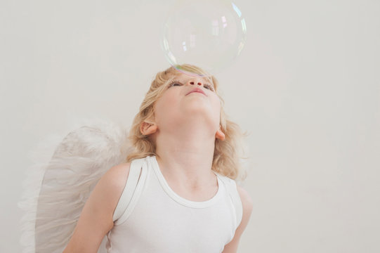 Portrait of little boy with angel wings blowing a soap bubble