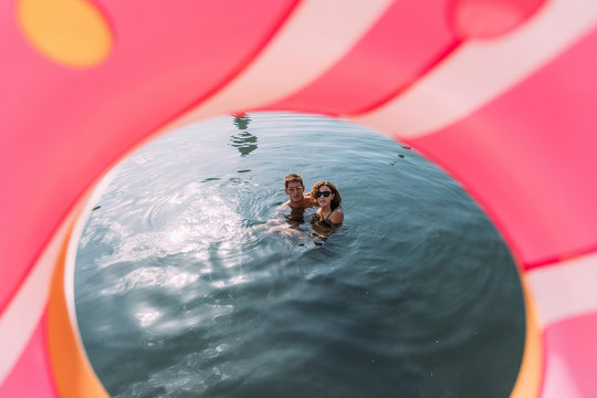 Young couple bathing in the sea behind inflatable float in donut shape