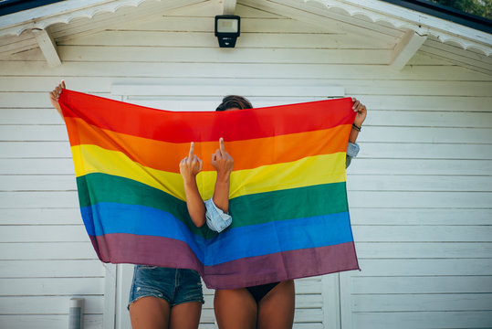 Two women giving the finger in front of a rainbow flag