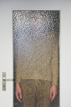 Man standing behind closed door with ribbed glass pane