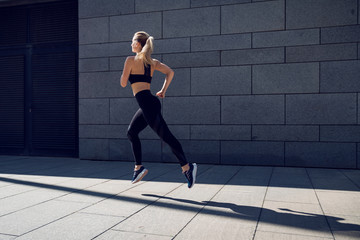 Woman in black sportswear jogging outdoors in front of dark wall