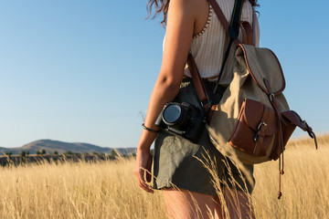 Young woman with a backpack and a camera in a meadow at sunset
