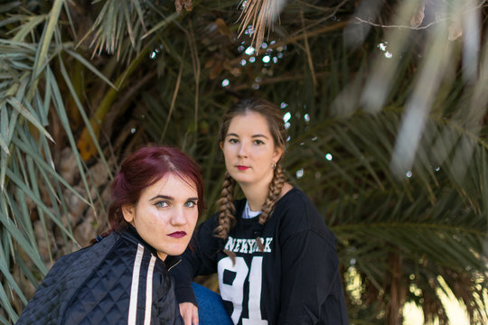 Two women are posing with palm trees in the background