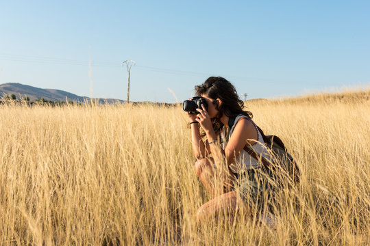 Young woman taking a picture with a camera in a meadow at sun