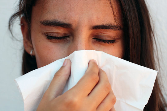 Young woman blowing nose into tissue