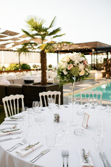 White table setting with floral centerpiece at outdoors wedding reception.