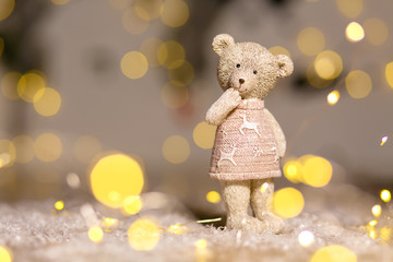 Decorative figurines of a Christmas theme. Figurine of a cute teddy bear girl in a sweater with deers. Festive decor, warm bokeh lights.