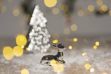 Decorative figurines of a Christmas theme. Statuette of a lying deer near a Christmas tree. Festive decor, warm bokeh lights. © Kate