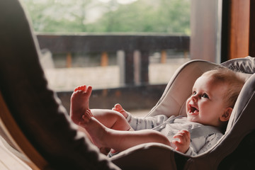 6 months baby girl sitting in a car seat near the panoramic window