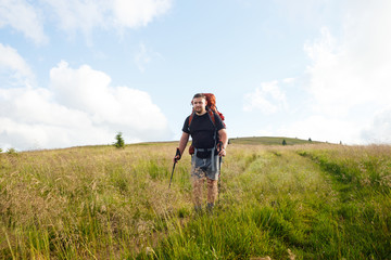 Man in a black t-shirt with a red backpack and trekking poles