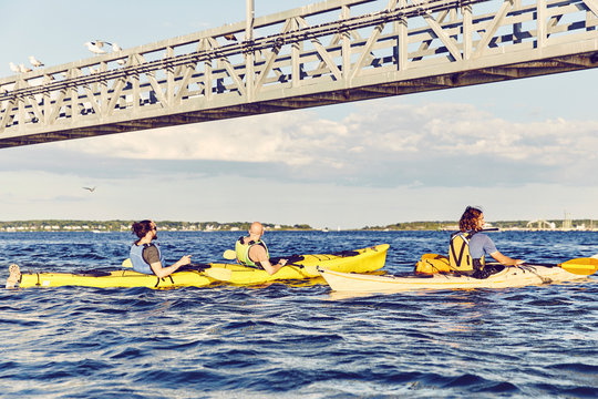 Group of kayakers paddle under a bridge at sunset in Casco Bay, Maine