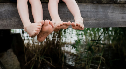 Two pairs of little sandy feet dangling off a pier at the beach