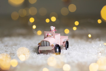 Decorative figurines of a Christmas theme. Santa statuette rides on a toy car with a trailer for gifts. Festive decor, warm bokeh lights.