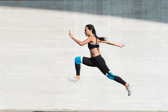 Full body of female athlete in sportswear jumping on concrete
