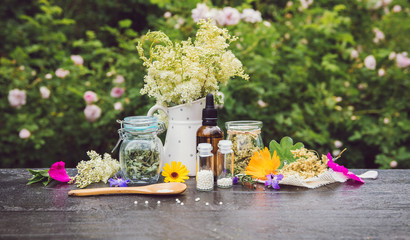 Homeopathic medicine pills on wood table, globules in jars and on wood spoon, decorated with fresh...