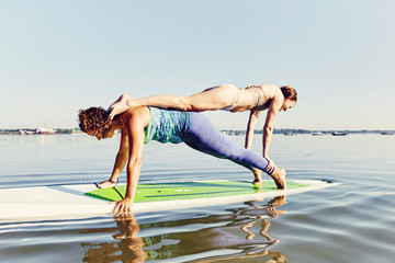 Two young women doing yoga on a standup paddle board