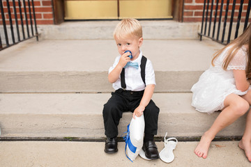 Ring bearer baby sits next to flower girl on steps and looks at camera