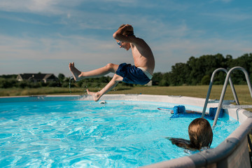 Young boy jumps into pool on a sunny summer day in the backyard