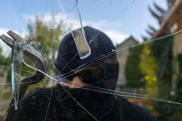 Burglar breaks the window. Burglar with obscured face trying to break the window