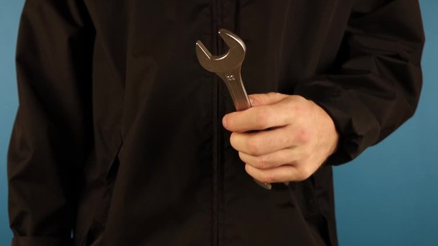 a man in black holds a wrench in his hand against a blue background