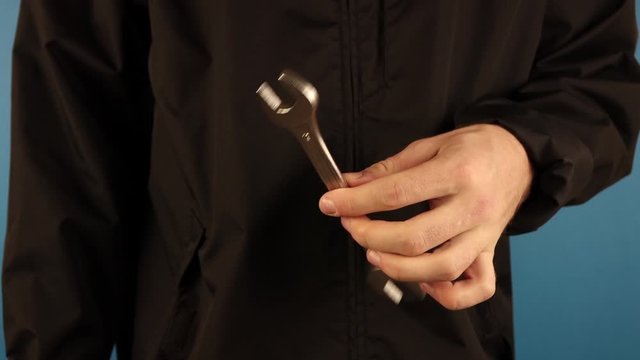 a man in black holds a wrench in his hand against a blue background
