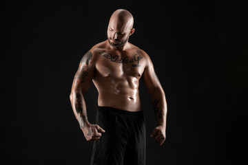 Fototapeta premium Athletic bald, bearded, tattooed man in black shorts is posing against a black background. Close-up portrait.