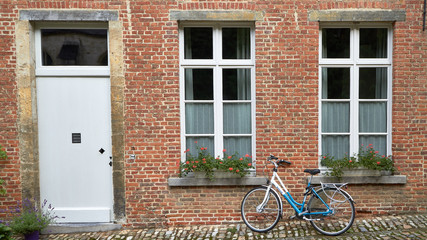 Fototapeta na wymiar Bicicleta apoyada en la pared de una casa de ladrillo con ventanas y jardineras de flores